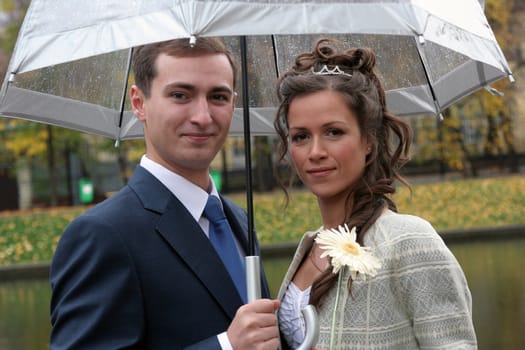 The groom and the bride under an umbrella in rainy weather