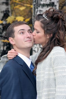 The bride kisses the groom in park in the autumn