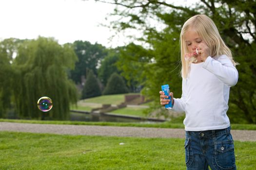 Pretty blond girl in the park blowing soapbubbles