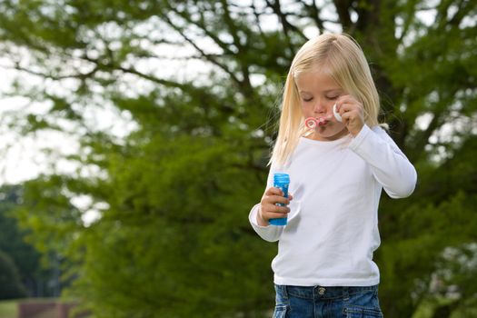 Cute little four year old girl blowing soapbubbles in the park