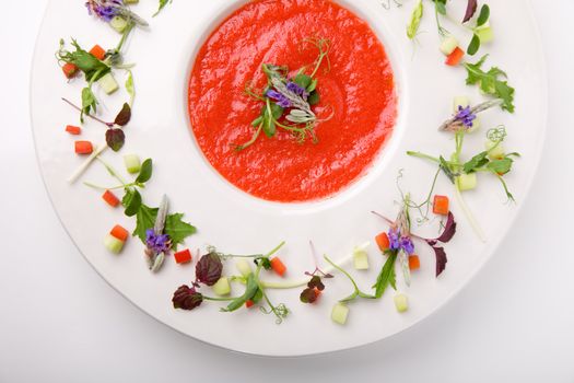 Dish filled with bright red cazpacho soup with decorated plate