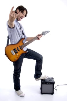 young rock star holding guitar with one leg on speaker against white background