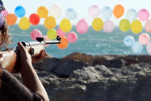 Women shooting a gun for colored balloons on background with sea