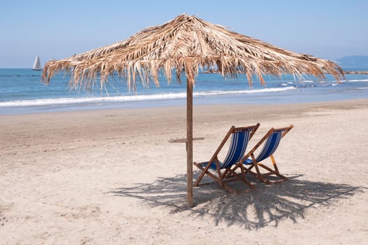 An empty beach with two beach chairs under a beach umbrella