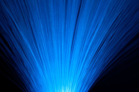 Close up capturing many vibrant blue fibre optic light strands arranged over black.