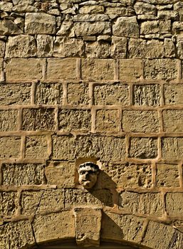 Gargoyle on a richly textured and eroded limestone wall in Malta
