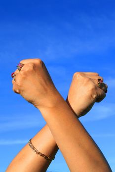Woman's hands showing power sign over blue sky.
