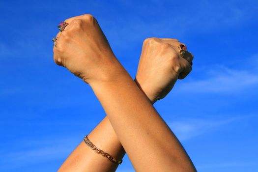 Woman's hands showing power sign over blue sky.
