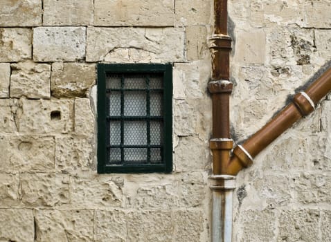 Little window and old drain pipes on eroded wall