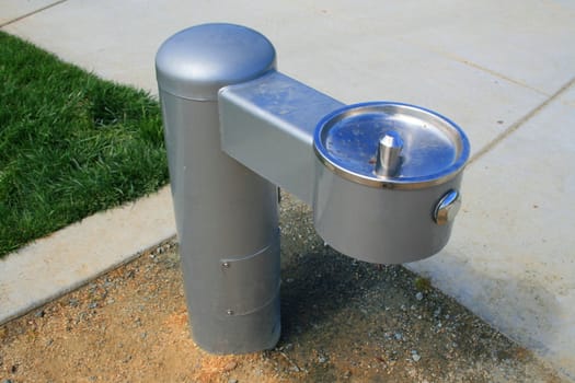 Drinking fountain on a sidewalk in a park.
