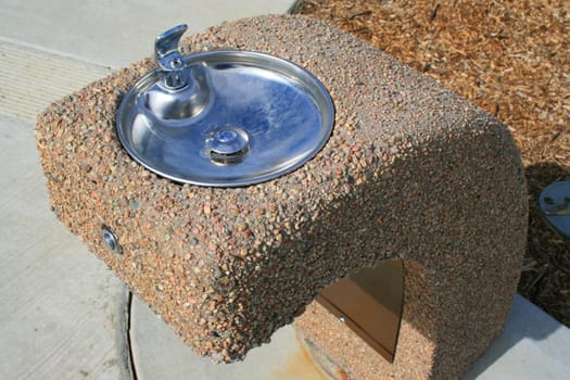 Drinking fountain on a sidewalk in a park.
