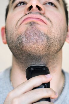 A closeup of a young man shaving his beard off with an electric shaver.