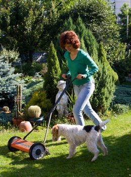 Girl with lawn mover and a small dog in the garden