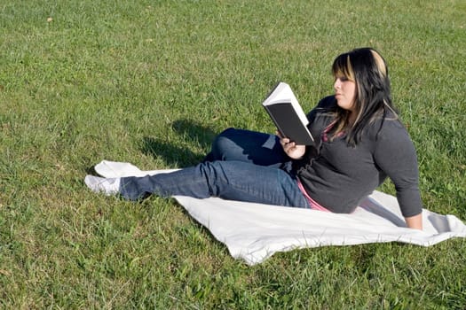 A young woman with highlighted hair reading a book or doing homework on campus.