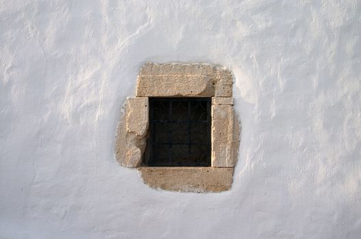 small window with grate in white lime wall