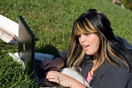 A young student using her laptop computer while laying in the grass on a nice day.