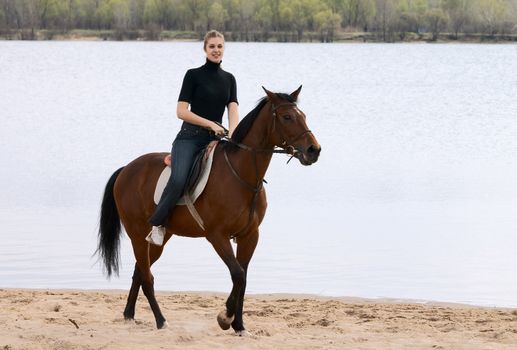 Blonde girl riding on horse at the beach