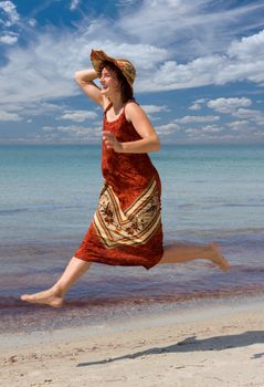 laughing girl in hat running and jumping at sea shore