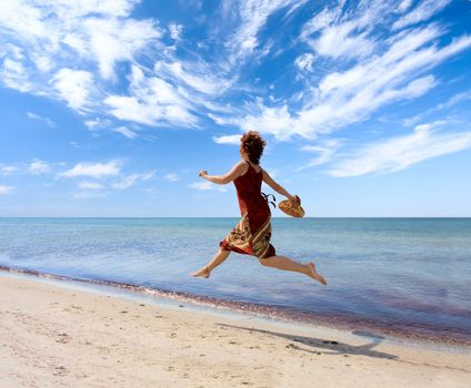 Woman running along the sea coast with hat in hand