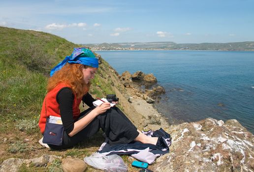 Girl with binoculars sitting on the rock making observations and taking notes 