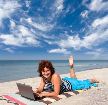 smiling girl working on laptop computer at sand sea coast