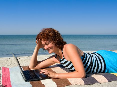 Smiling girl woking on laptop computer at sea beach