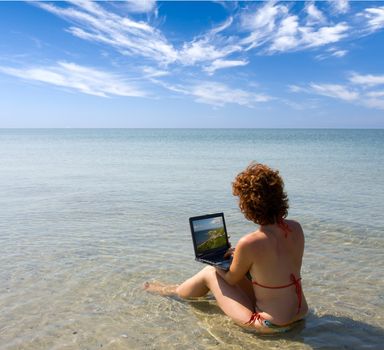 Girl with laptop computer sitting in water at seaside