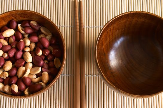 Wooden noggin with peanuts and empty one on the bamboo mat