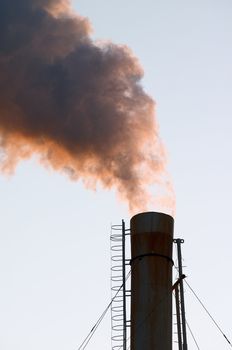 Smokestack throwing out puffs of orange smoke