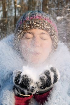 Girl in blue fur blowing the snow from her hand