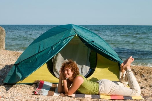 Smniling girl lie near of her tent at seaside