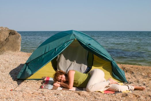 red-haired woman sleep near of a tent at seaside