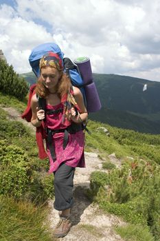 Backpacker girl going by path in a mountains