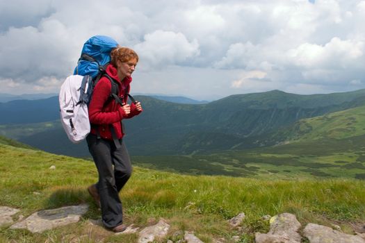 Hiker girl with backpack going by track on mountains
