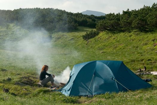 Girl siting near of a tent and making a campfire