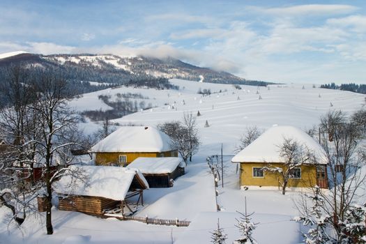 Houses under snow sarrunded by hilly landscape  