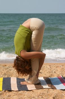 girl doing Uttanasana yoga pose at sea coast