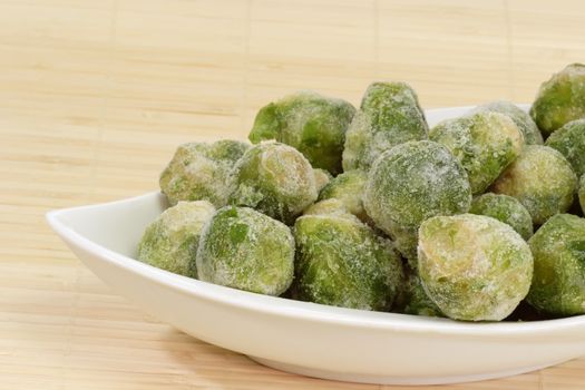 Frozen Brussels sprouts in a bowl on bright background