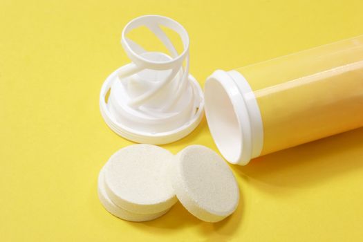 Effervescent tablets with plastic container on yellow background