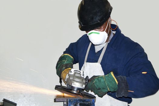 A man wearing protective gear, grinding a piece of metal in a factory