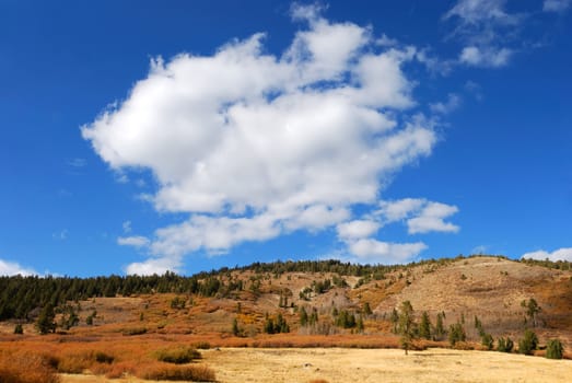 White cloud in blue sky above mountain side