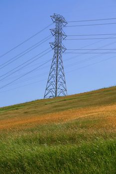 Electricity pylon on a hill over clear blue sky.
