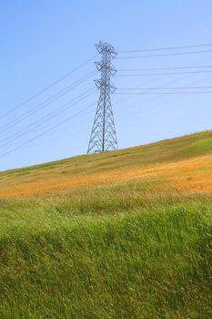 Electricity pylon on a hill over clear blue sky.
