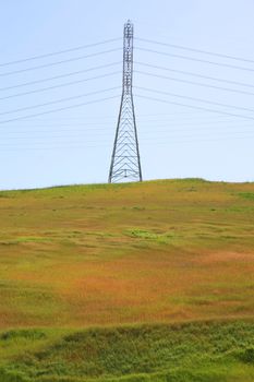 Electricity pylon on a hill over clear blue sky.
