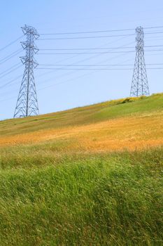 Two electricity pylons on a hill over clear blue sky.
