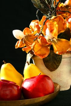 Red apples and yellow pears on a brass platter next to a vase with vivid flowers.
