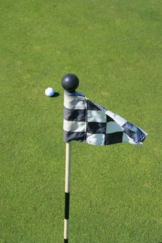 Close up of a golf course flag and a golf ball.
