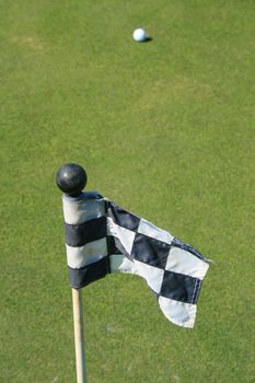 Close up of a golf course flag and a golf ball.
