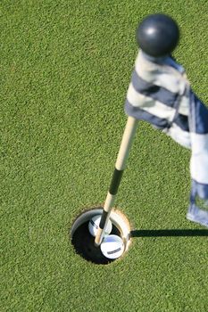 Close up of a golf course flag and two golf balls.
