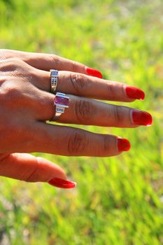 Woman's hand with gold rings over green grass.
